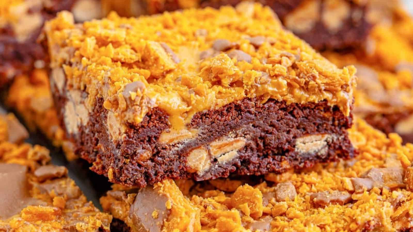 Close-up of a rich chocolate brownie topped with crunchy golden toffee bits and chocolate chips, showcasing its layered texture.