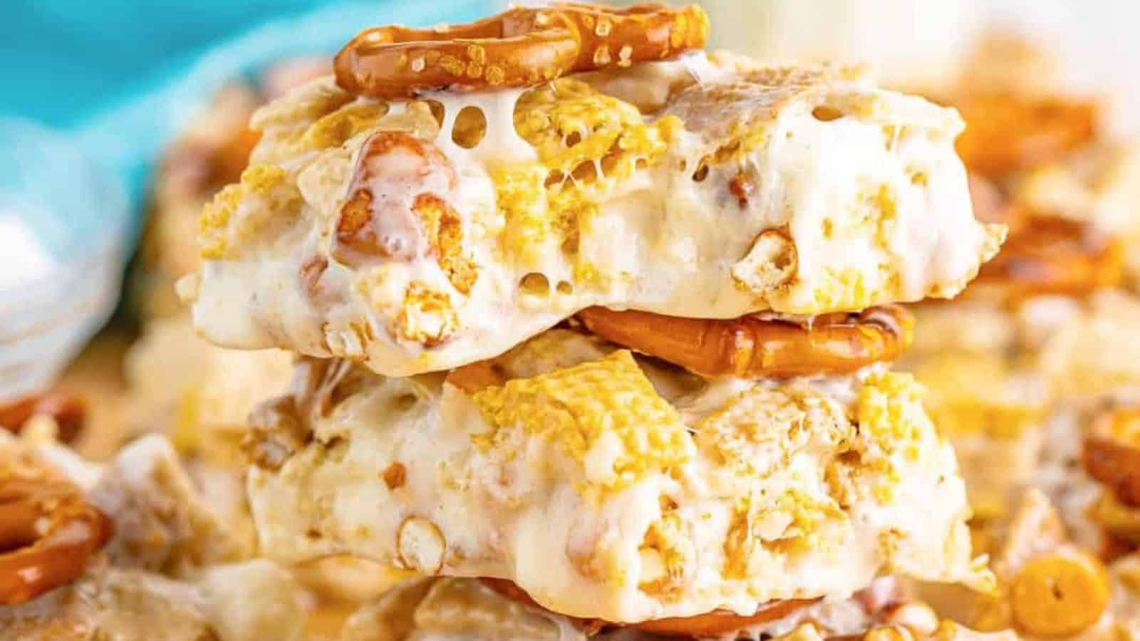 A close-up of stacked treats made with gooey marshmallow, pretzels, and cereal, drizzled in melted sweetness.