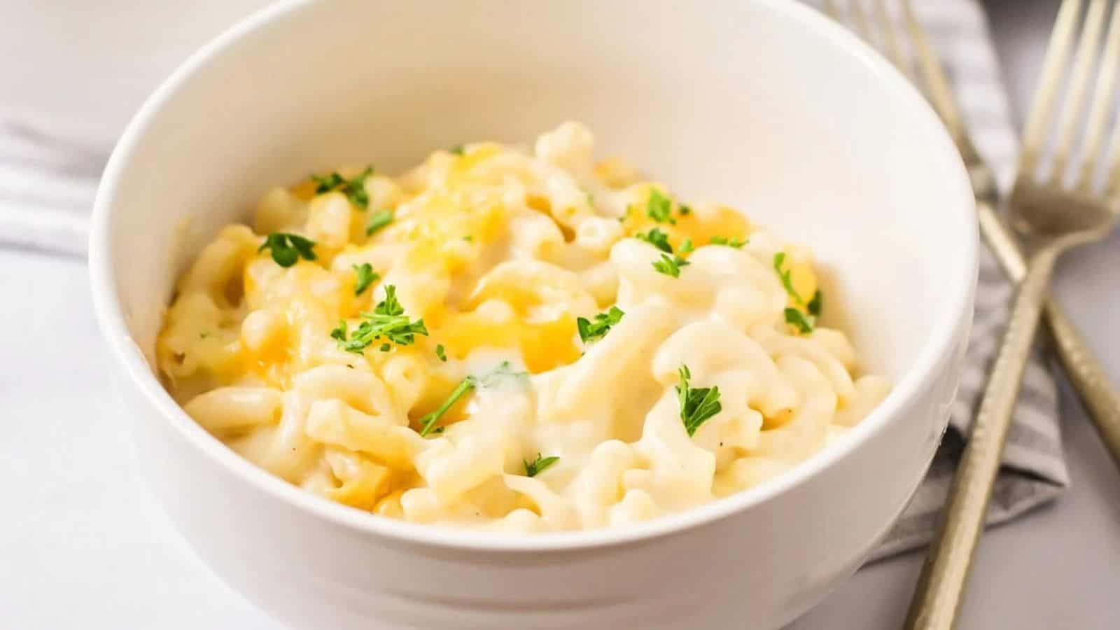 A creamy bowl of macaroni and cheese, topped with melted cheese and garnished with fresh parsley, served with gold forks beside it.