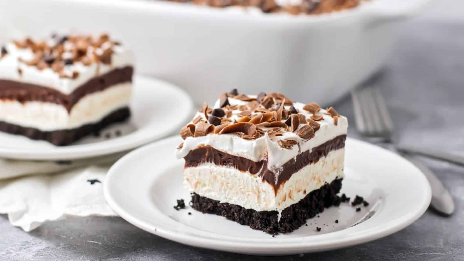 Layered chocolate dessert with an Oreo crust, topped with whipped cream and chocolate shavings on a white plate.
