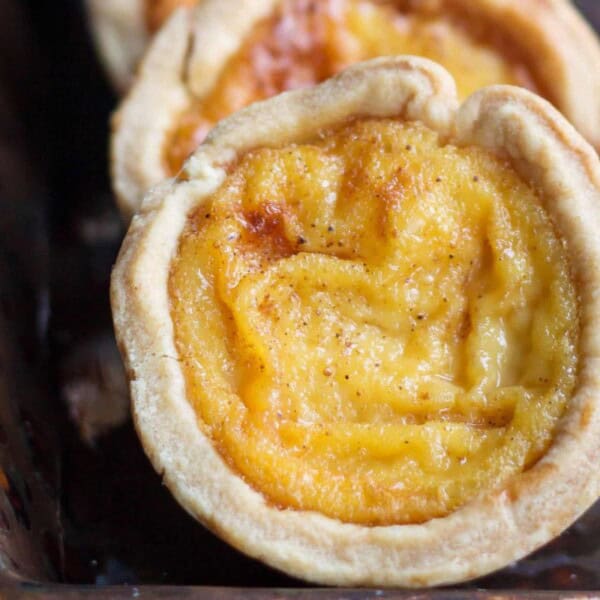 A close-up of golden, creamy egg custard tarts in flaky pastry shells, arranged on a decorative tray.