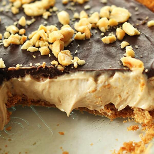 The image shows a pie with a slice removed, displaying its creamy filling and chocolate topping, and sprinkled with crushed nuts.