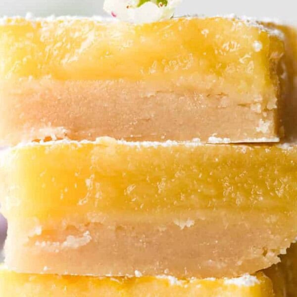 Three stacked lemon bars with a dusting of powdered sugar on top sit in front of a blurred background.