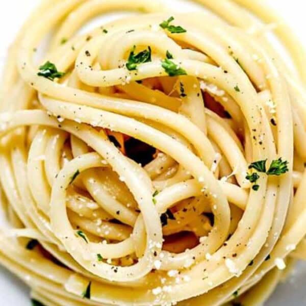 A serving of spaghetti pasta topped with parsley, black pepper, and grated cheese on a white plate.
