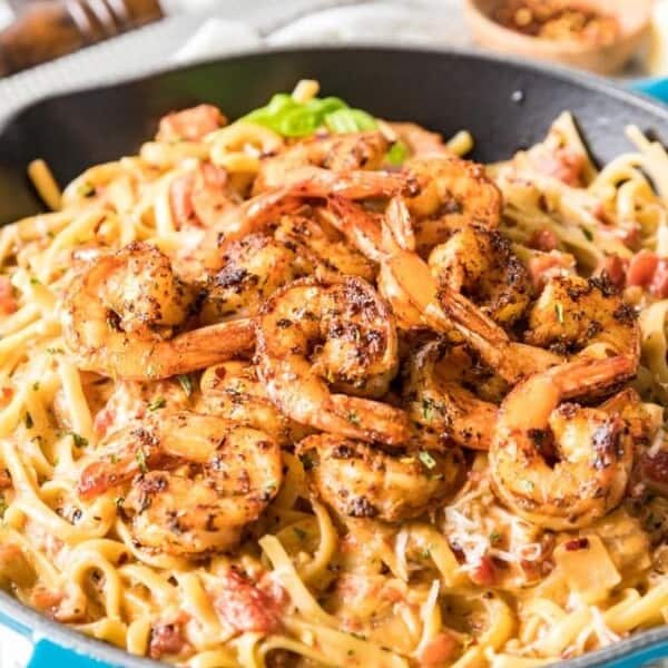 A blue skillet containing grilled shrimp and pasta in a creamy sauce, garnished with herbs. Served with