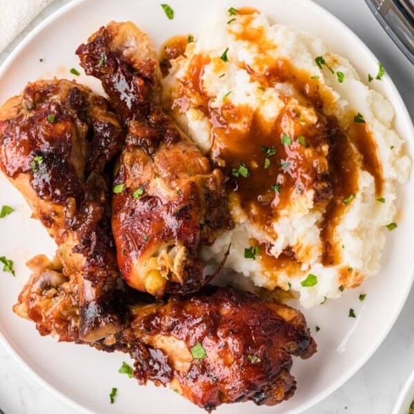 Plate with barbecued chicken drumsticks, mashed potatoes with brown gravy, and chopped herbs.