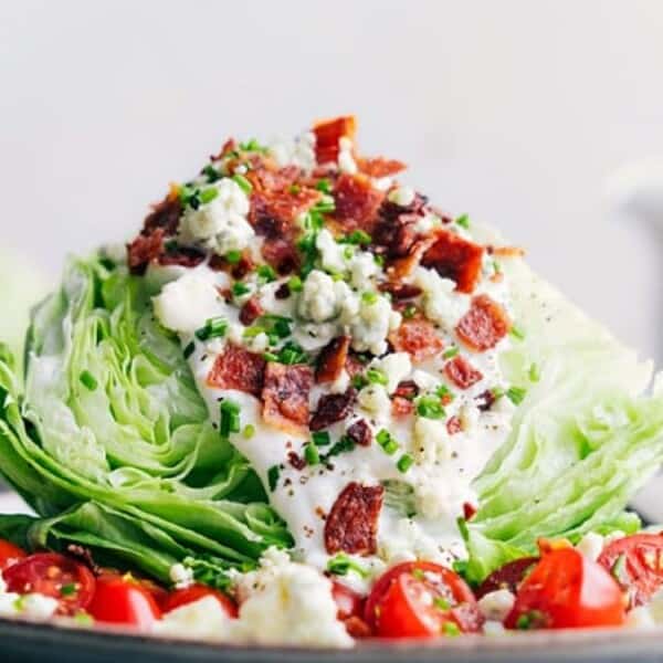 The image features a wedge salad topped with bacon bits, blue cheese, chives, and cherry tomatoes.