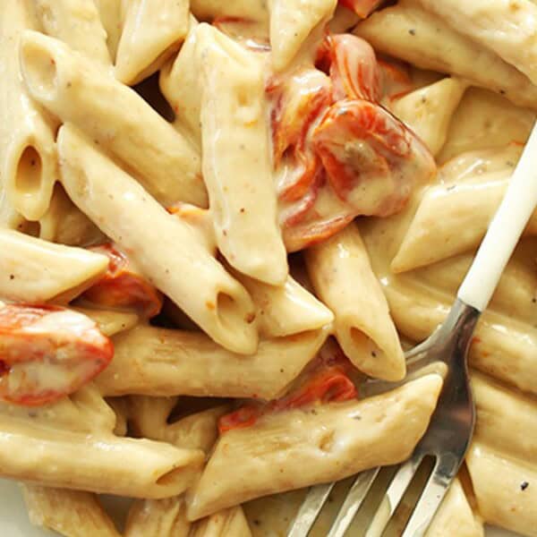 A plate of penne pasta with a creamy sauce and roasted cherry tomatoes.