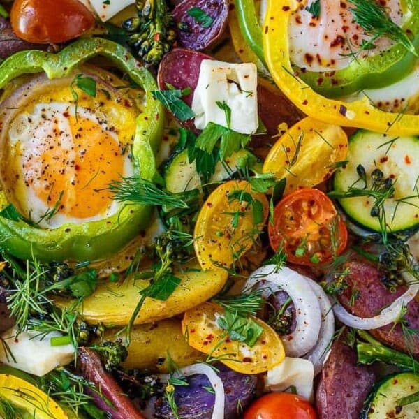 The image features baked eggs nestled in bell pepper rings, surrounded by assorted vegetables including zucchini slices, cherry tomatoes, and red onion pieces, all garnished with herbs on a baking tray.