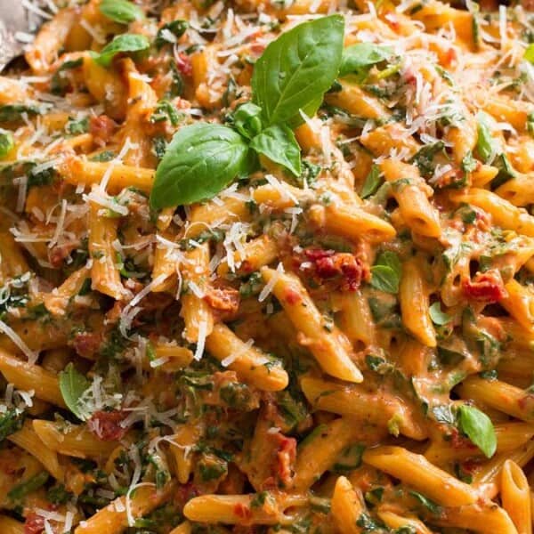 A plate of penne pasta with creamy tomato sauce, topped with grated cheese and basil leaves. A fork and spoon are placed beside the plate.