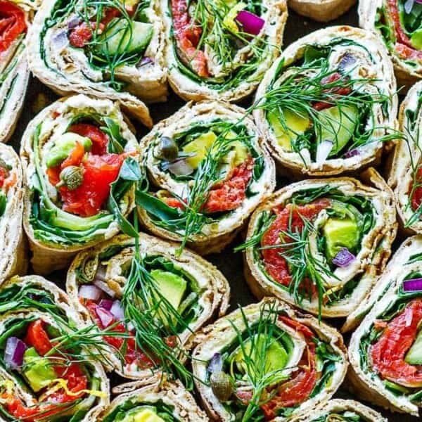 Colorful vegetable wraps filled with tomatoes, cucumbers, spinach, and dill are arranged on a dark plate.