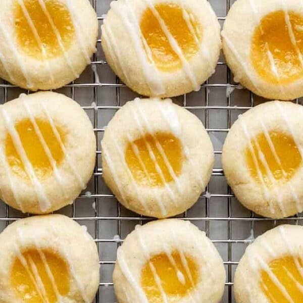 The image shows rows of lemon thumbprint cookies on a wire rack, each topped with a drizzle of white icing.