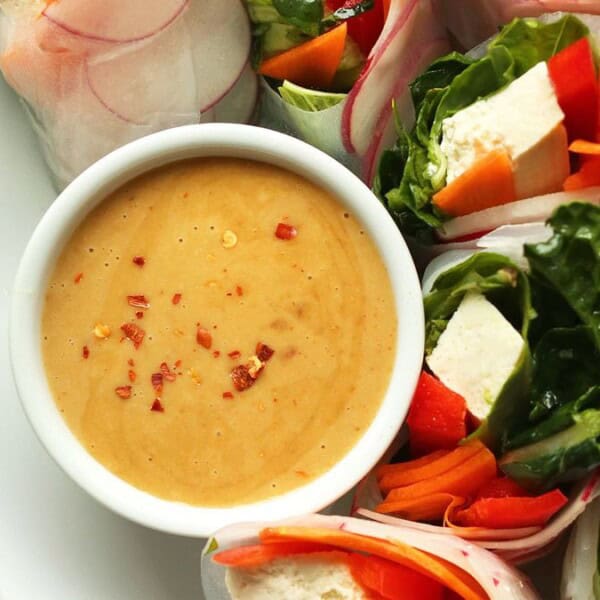 A plate featuring fresh vegetable spring rolls and sliced tofu, accompanied by a bowl of creamy dipping sauce and garnished with red pepper flakes; lime wedge on the side.