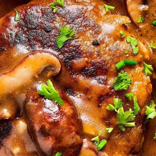 A Salisbury steak covered in mushroom gravy and garnished with chopped parsley. Served with