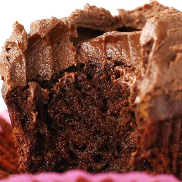 A partially eaten chocolate cupcake with creamy frosting in a pink paper liner.