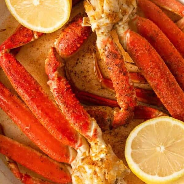 Cooked crab legs seasoned with spices in a white dish, garnished with two lemon halves.
