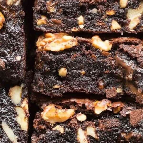 Close-up of freshly baked brownies with walnuts, neatly arranged in a paper-lined tray. The rich, dark chocolate surface is interspersed with golden walnut pieces, creating a textured and appetizing appearance.