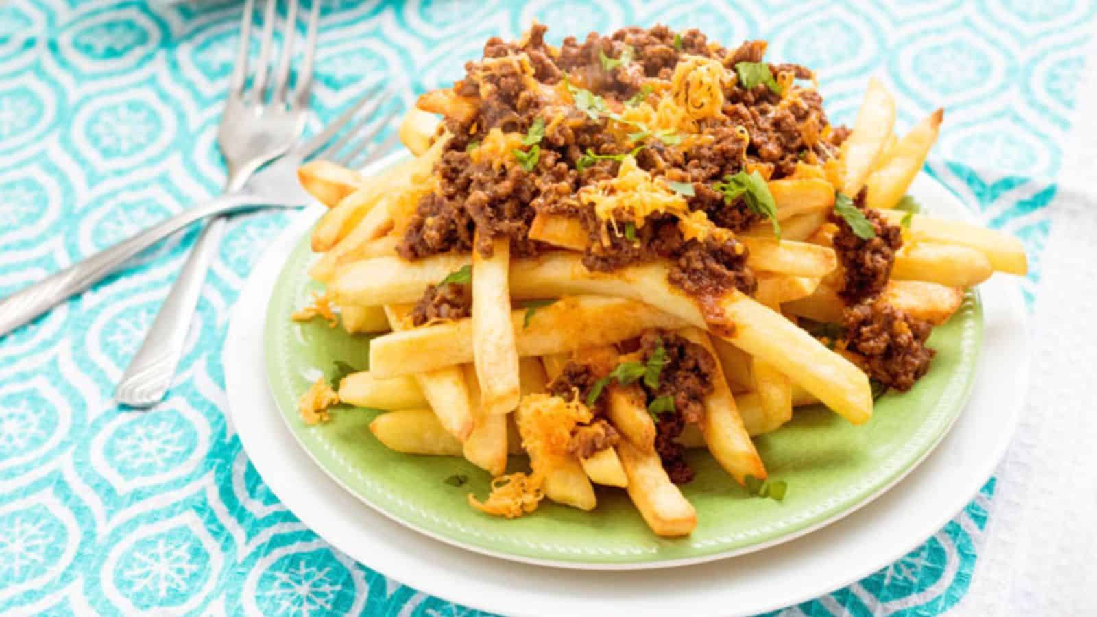A heaping plate of French fries topped with seasoned ground beef, melted cheese, and fresh herbs, on a green plate.