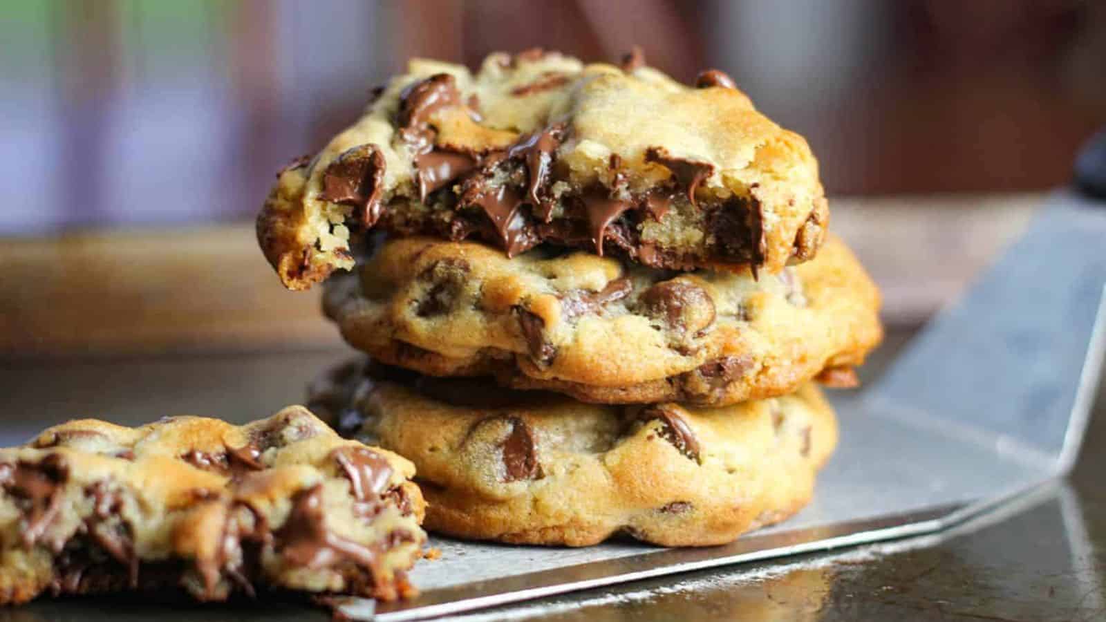 Three stacked chocolate chip cookies, with melted chocolate oozing from the top cookie, resting on a metal spatula.