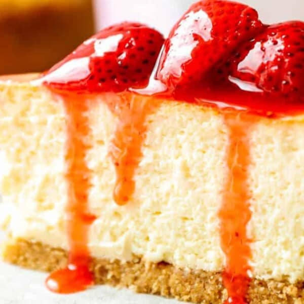 A slice of cheesecake topped with fresh strawberries and drizzled with strawberry sauce. Served with