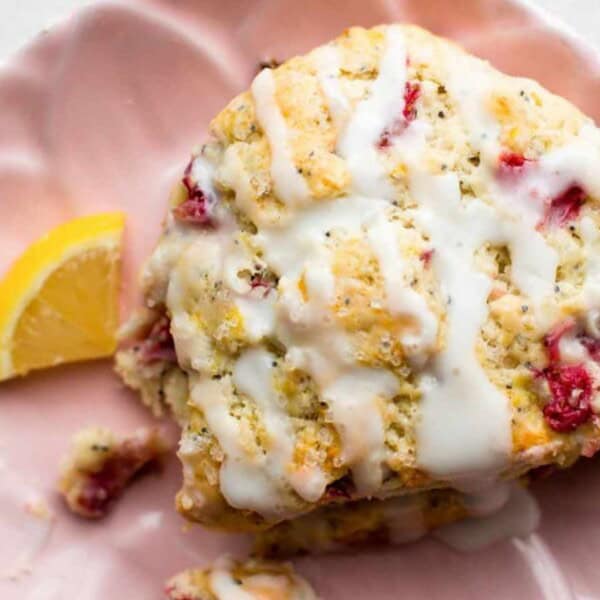 A lemon raspberry scone with white icing is on a pink plate, accompanied by a lemon wedge.