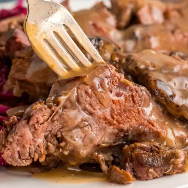 A fork piercing tender, sliced beef smothered in gravy, served alongside vibrant red cabbage on a plate.