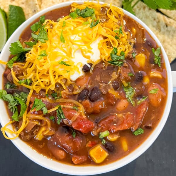A hearty bowl of chili topped with cheese, sour cream, and fresh cilantro, served with lime and tortilla chips on the side.