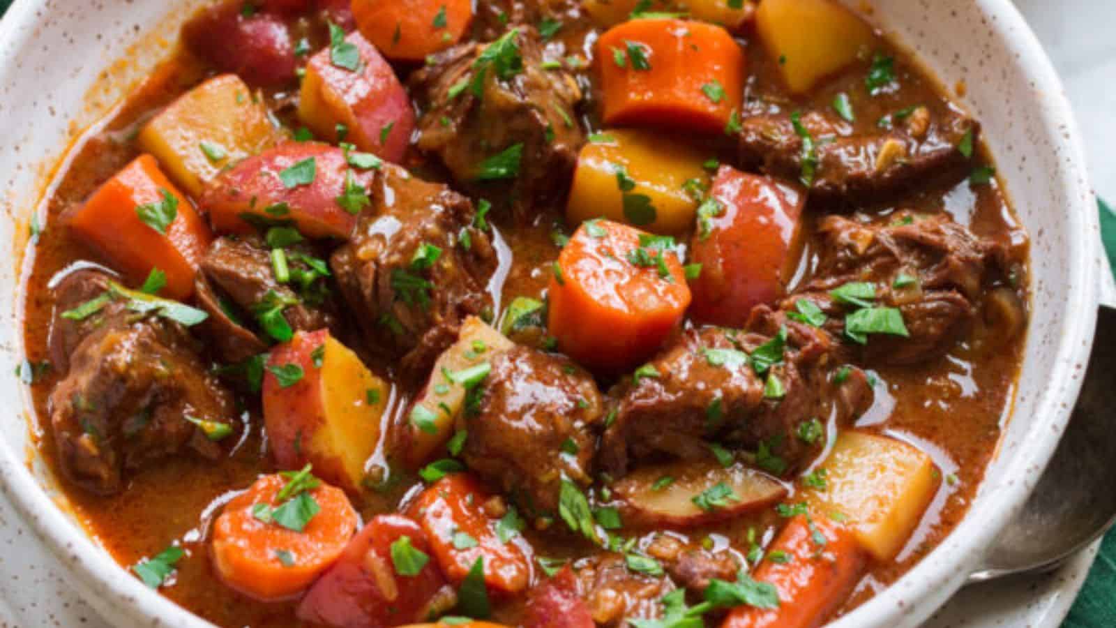 A bowl filled with chunks of beef, carrots, and potatoes in a brown broth, garnished with parsley.