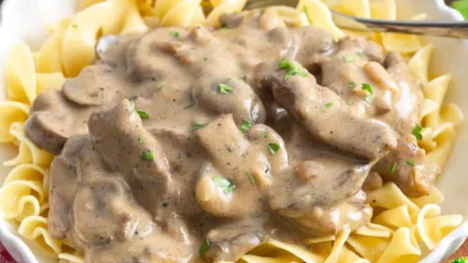 A plate of egg noodles topped with creamy beef and mushroom sauce, garnished with chopped herbs.