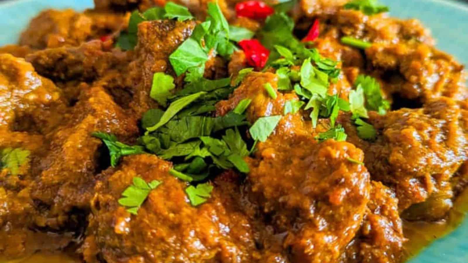 A plate of curry with chunks of meat, topped with chopped cilantro and red chili slices.