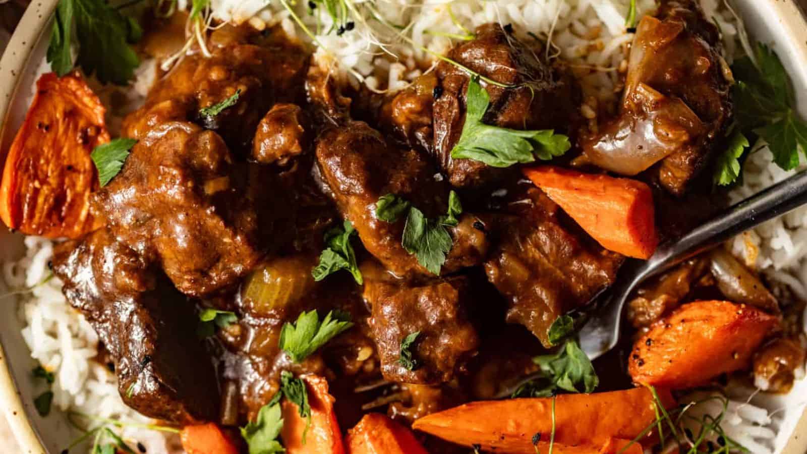 A plate of white rice topped with beef stew, cooked carrots, onions, and fresh parsley.