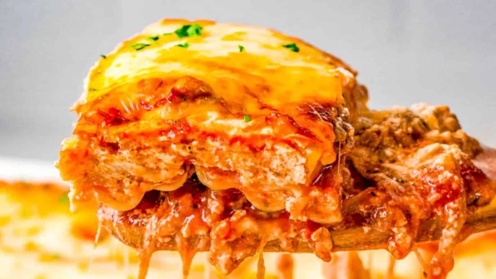 A slice of lasagna with visible layers of meat sauce and melted cheese, held on a wooden spatula.