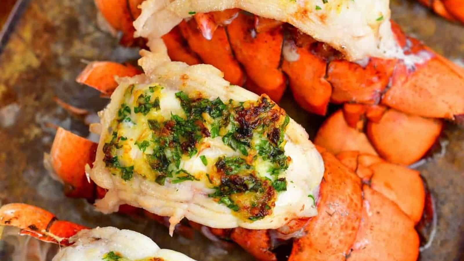 Baked lobster tails topped with melted herb butter and garnished with chopped parsley, arranged on a tray.