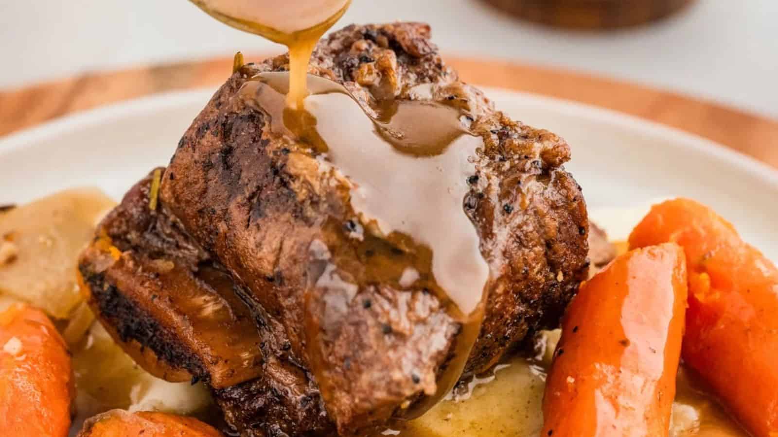 A piece of beef short rib topped with brown gravy, accompanied by cooked carrots on a plate.
