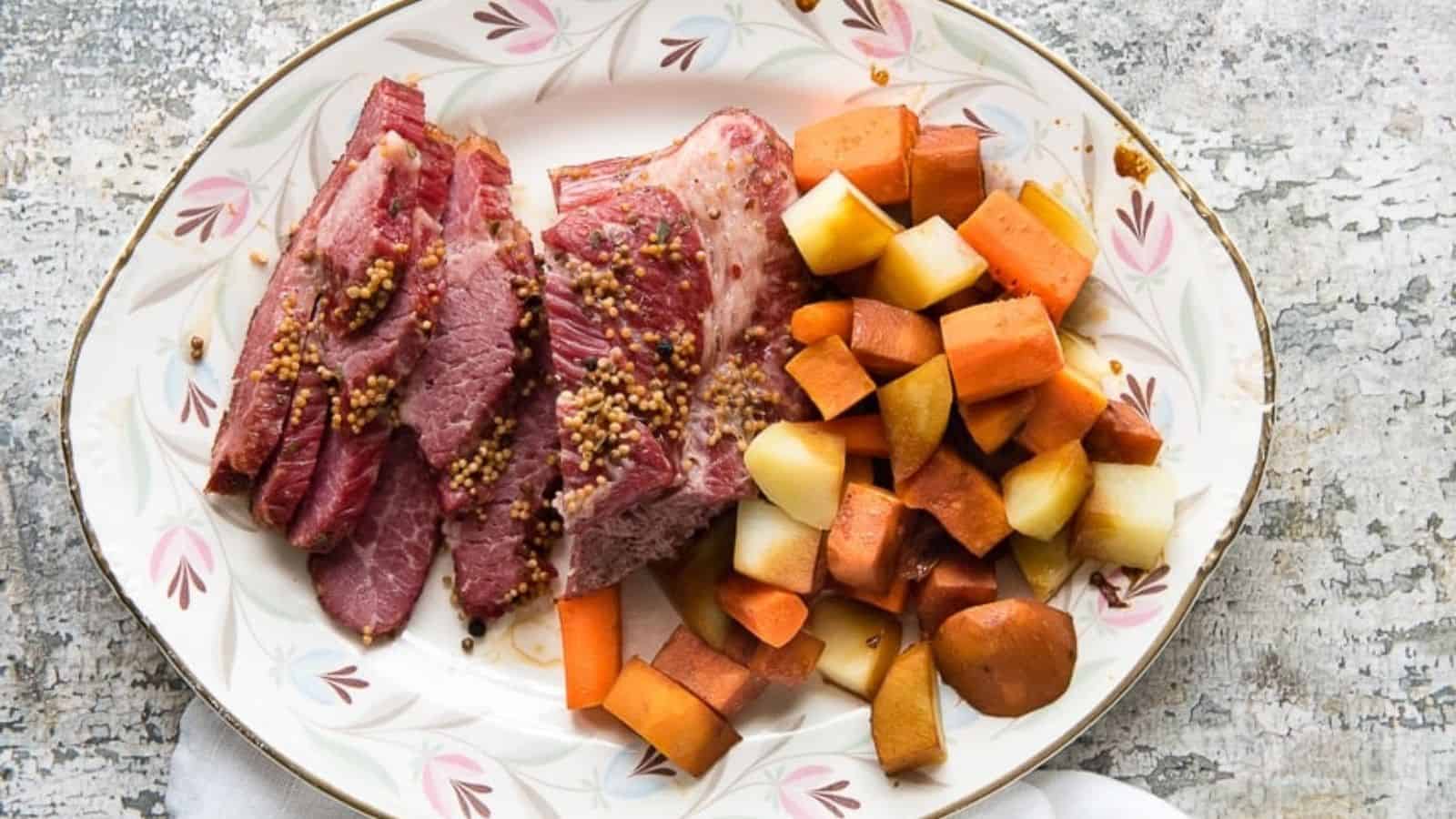 Sliced corned beef garnished with mustard seeds, accompanied by cooked potatoes and carrots on a plate.