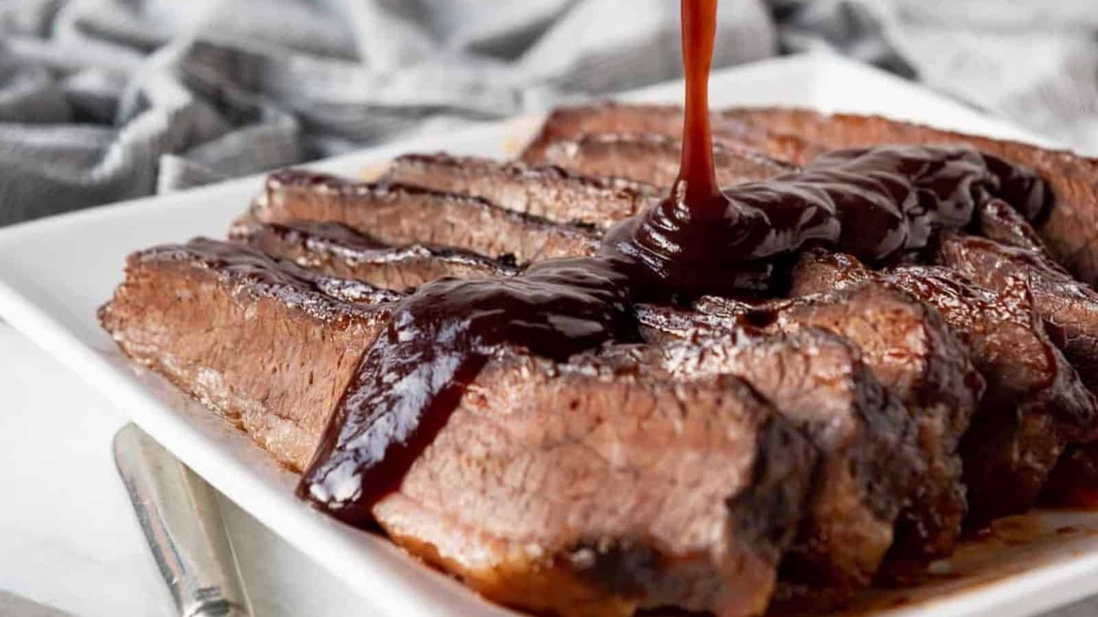 Slices of cooked brisket arranged on a white plate with barbecue sauce poured over them.