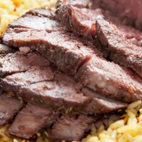 Slices of roast beef arranged on yellow rice, garnished with herbs and seasonings.