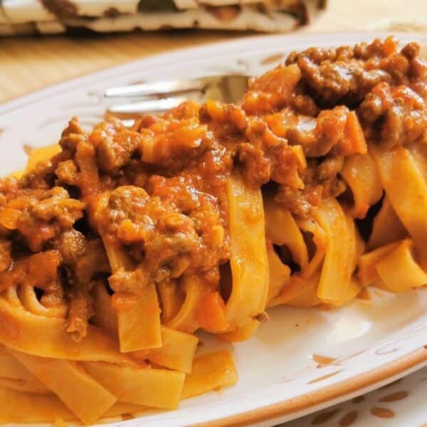 Tagliatelle pasta with a meat-based tomato sauce on a decorative oval plate.