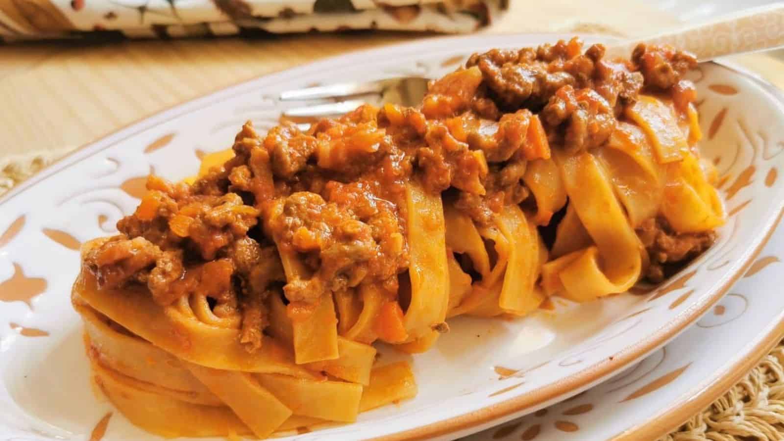 Tagliatelle pasta with a meat-based tomato sauce on a decorative oval plate.