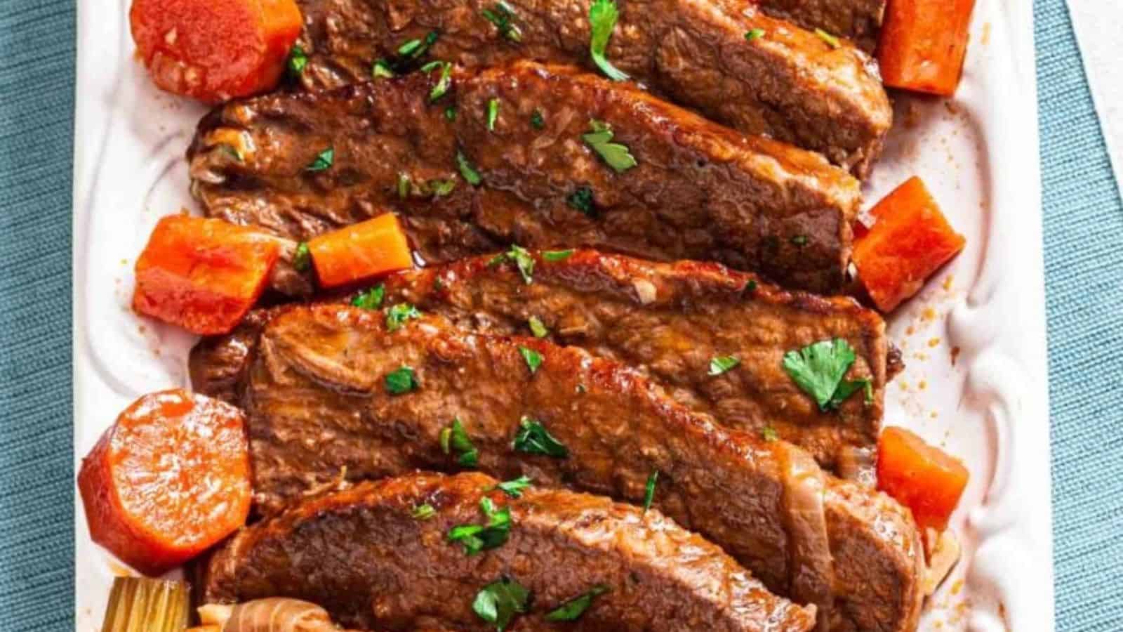 Slices of pot roast topped with chopped parsley, accompanied by chunks of carrots and celery, arranged on a white platter.