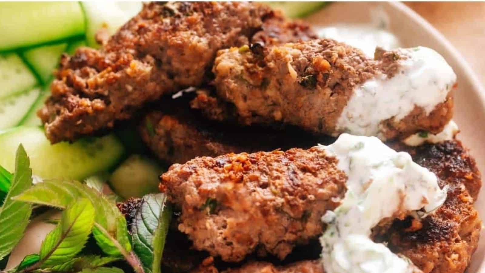 Kebab-style ground meat, sliced cucumbers, mint leaves, and a dollop of yogurt sauce arranged on a plate.