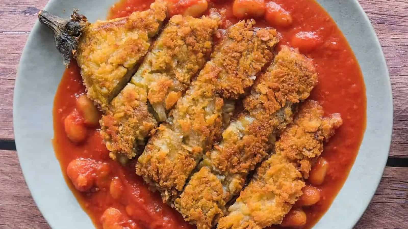 Sliced, breaded fried eggplant served on a plate with tomato sauce and white beans.