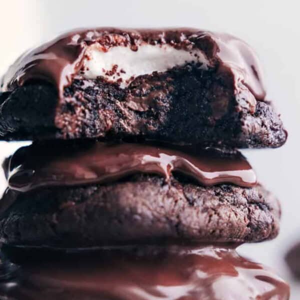 Stack of three glossy chocolate-coated treats; the top one has a bite missing, showing a white marshmallow filling inside.