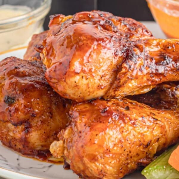 A plate of glazed chicken drumsticks with celery and carrots, accompanied by dipping sauces in the background.