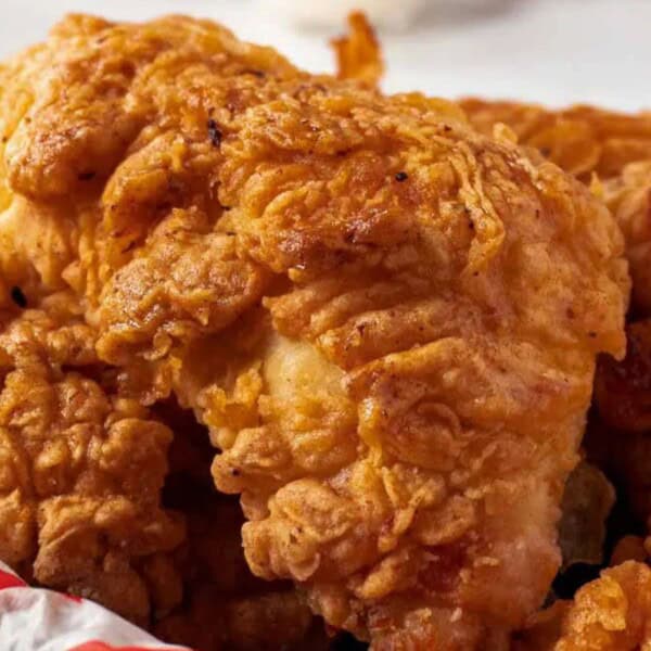Close-up of crispy fried chicken pieces resting in a red and white checkered basket, highlighting their golden, crunchy texture.