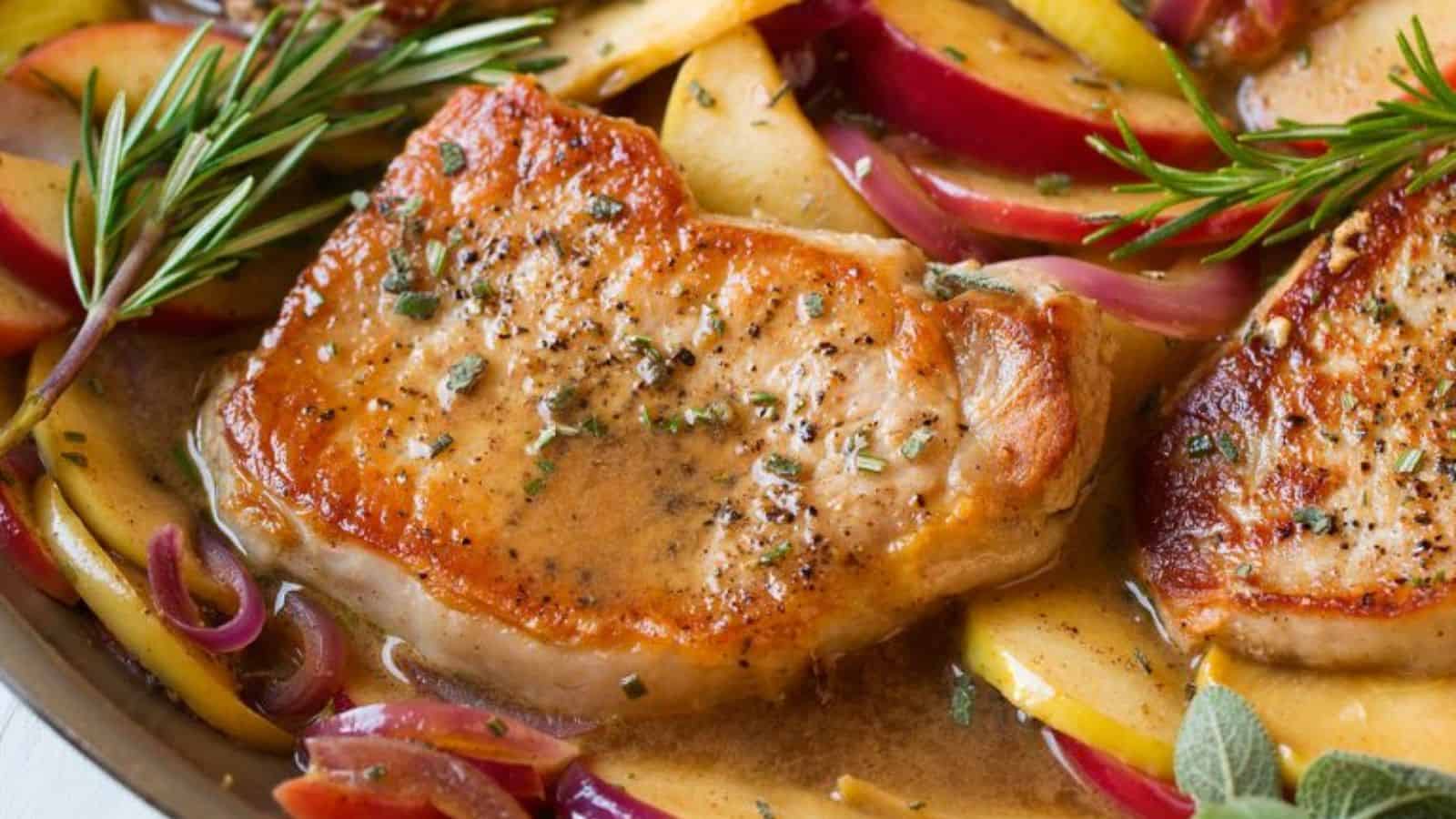 Sizzling pork chops with herbs, served atop sautéed apples and red onions, glistening in savory sauce.