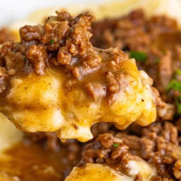 A close-up of a spoonful of creamy mashed potatoes topped with savory ground beef and gravy, garnished with parsley.