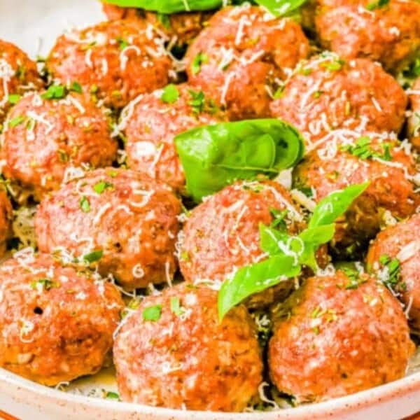 A bowl filled with freshly made meatballs, garnished with basil and shredded cheese, showcasing a delicious homemade dish.