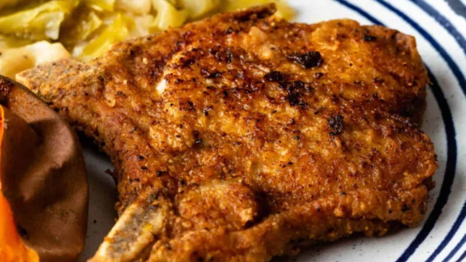 A golden-brown fried pork chop on a plate, accompanied by collard greens and a baked sweet potato.