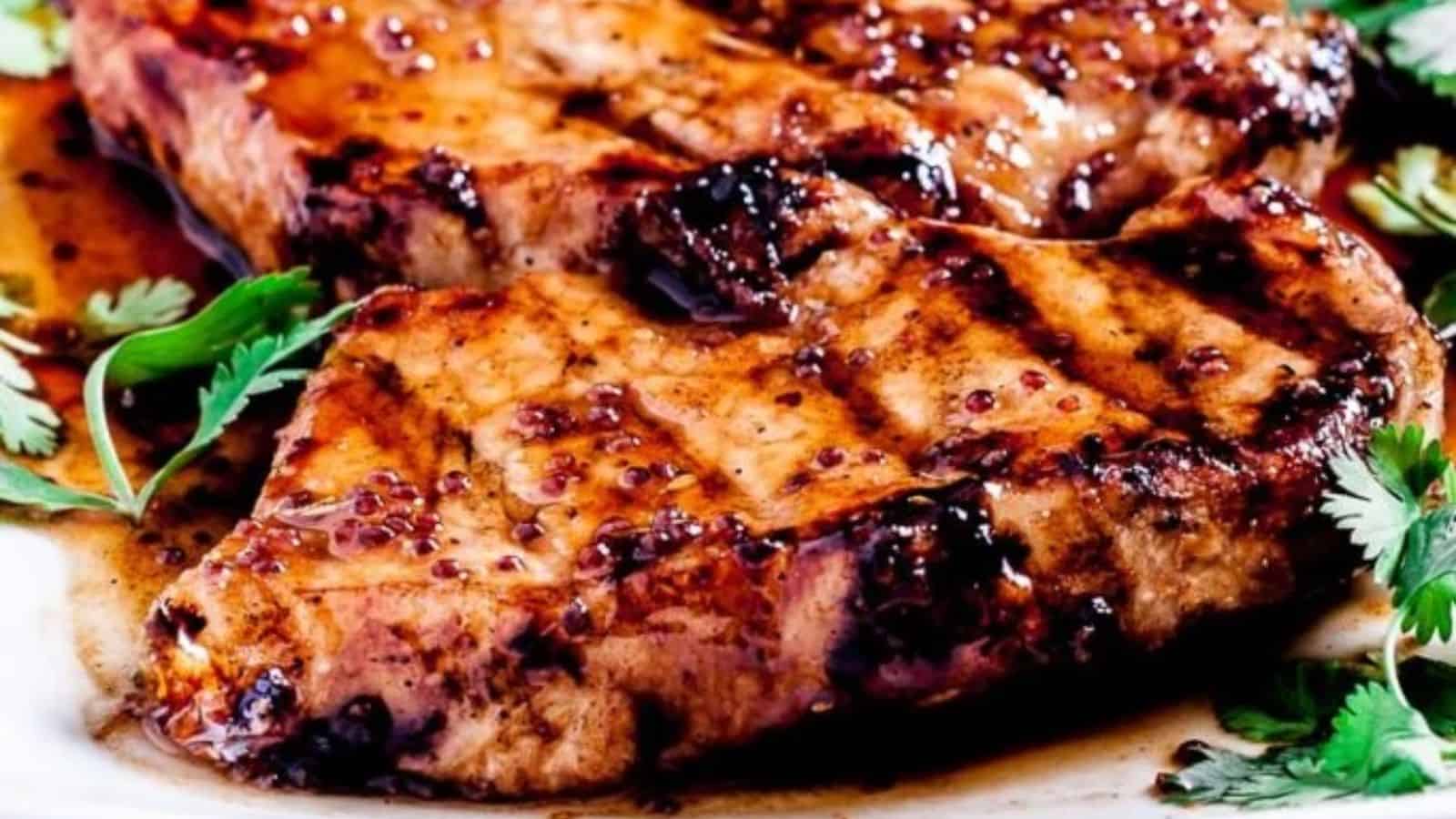 Two succulent grilled pork chops glazed in a rich sauce, garnished with fresh cilantro leaves.
